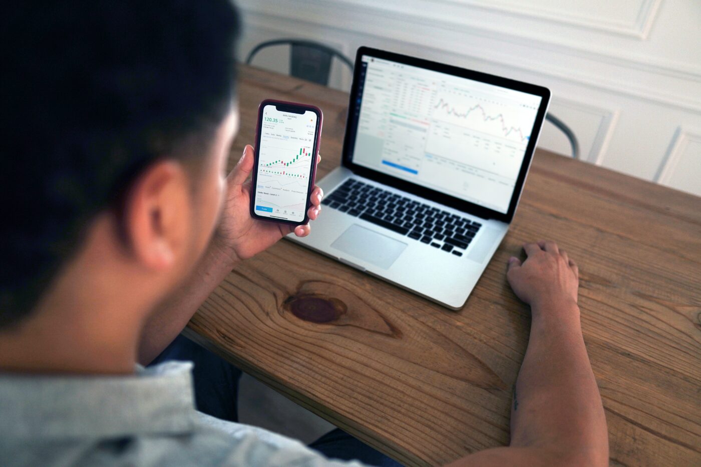 stocks.jpg Man looking at stock trades on his phone and laptop